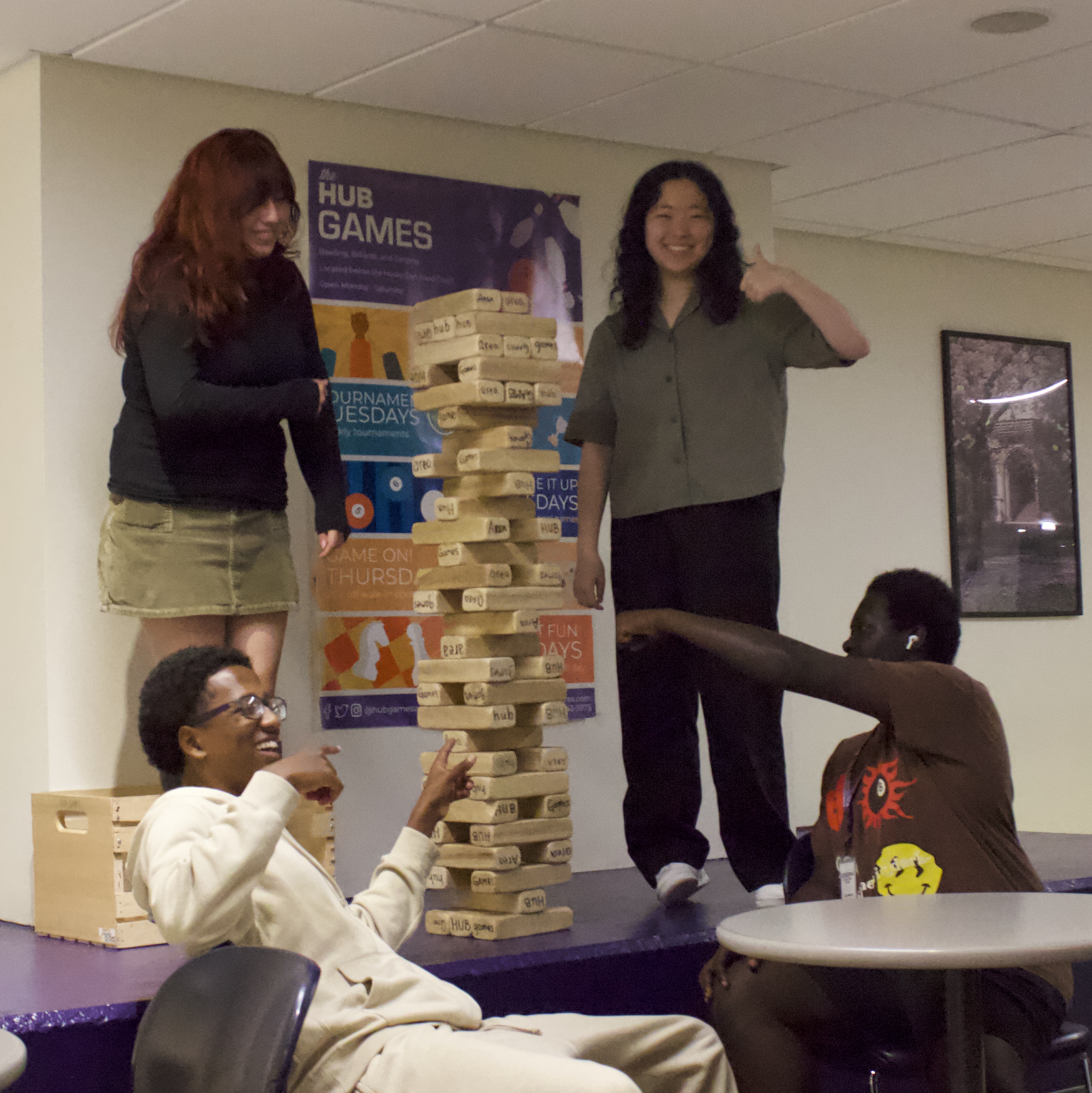 Two students standing on a raised ledge playing Jenga with large blocks with two more students sitting nearby