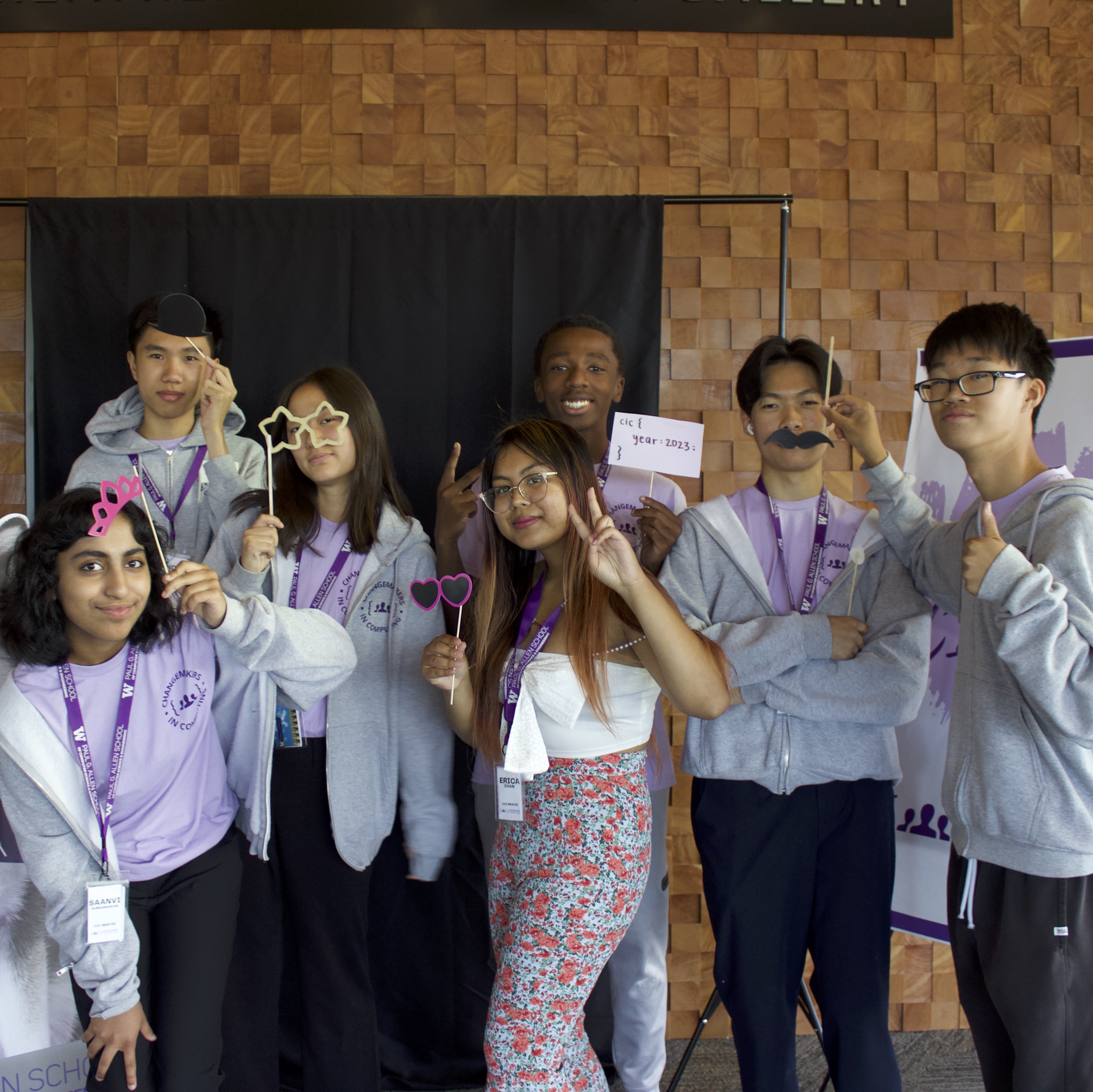 A group of 7 students some with photobooth props posing for the camera
