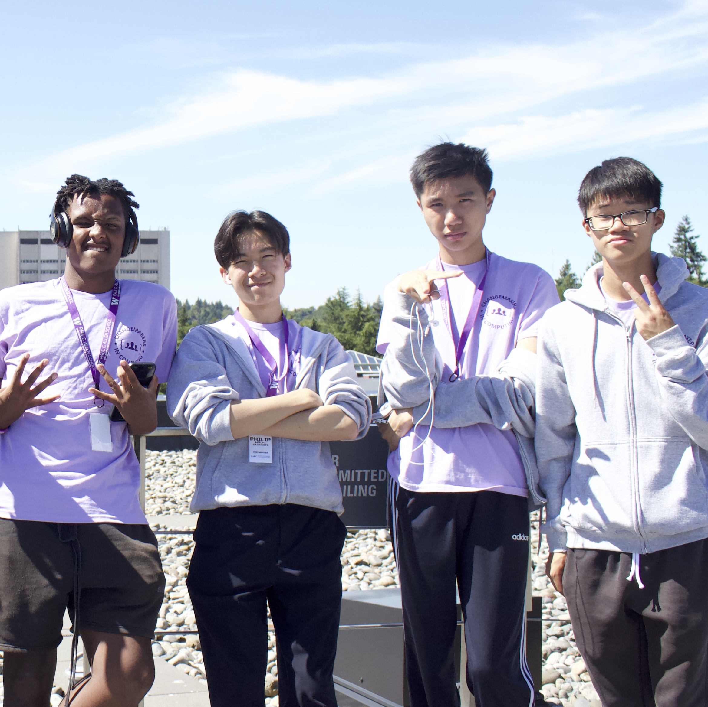 4 students in a relaxed pose showing peace signs with the open sky behind them