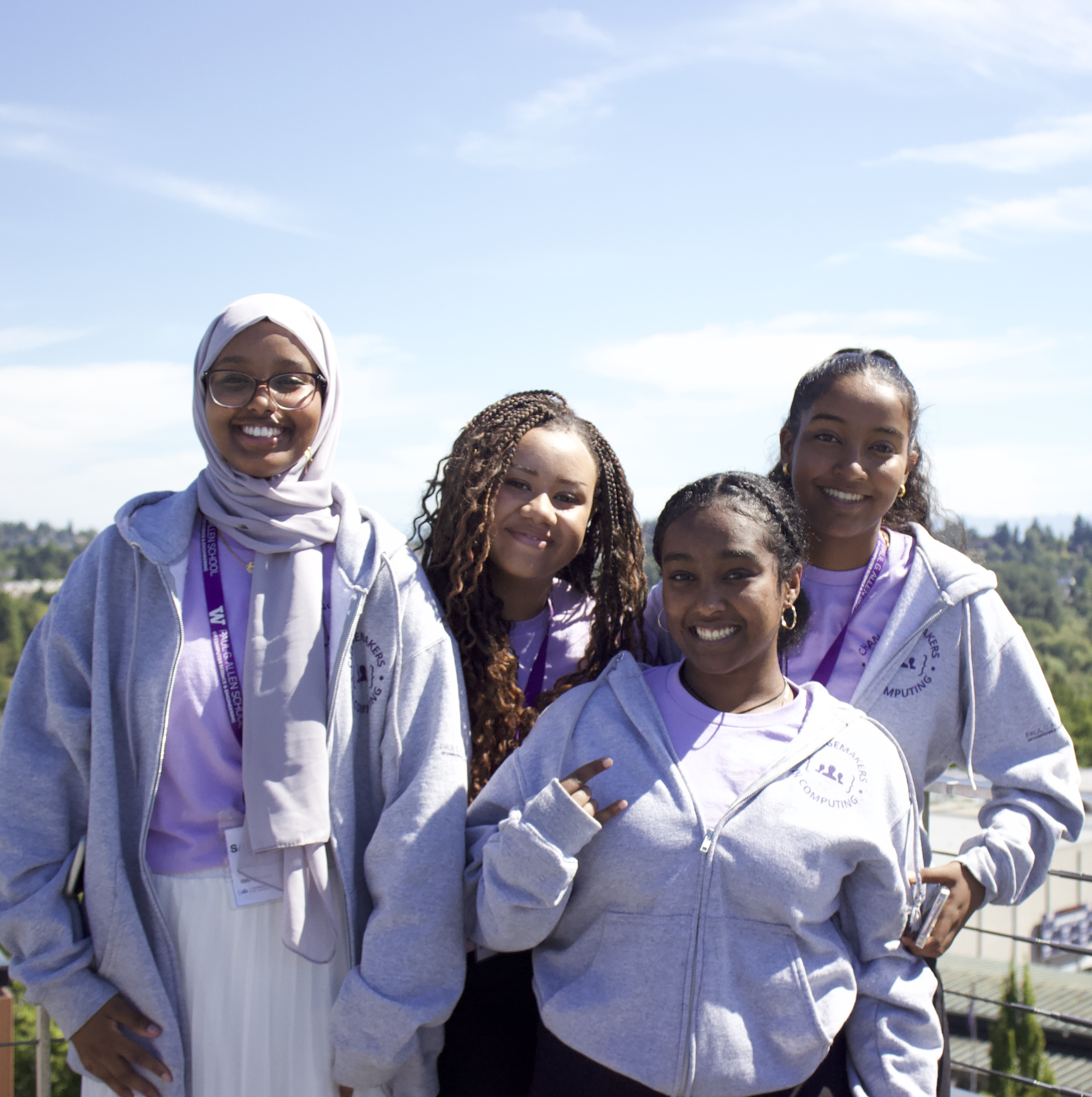 4 students smiling towards the camera with the open sky behind them