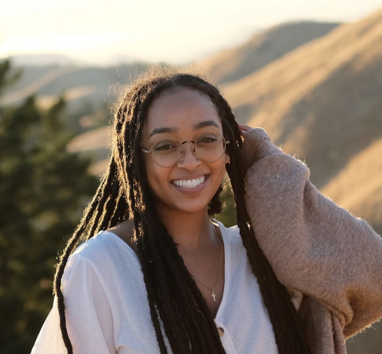 Headshot of Betania, an Ethiopian nonbinary femme in their early 20’s with black locs. She’s wearing a blouse, cardigan, glasses, and smiling at the camera