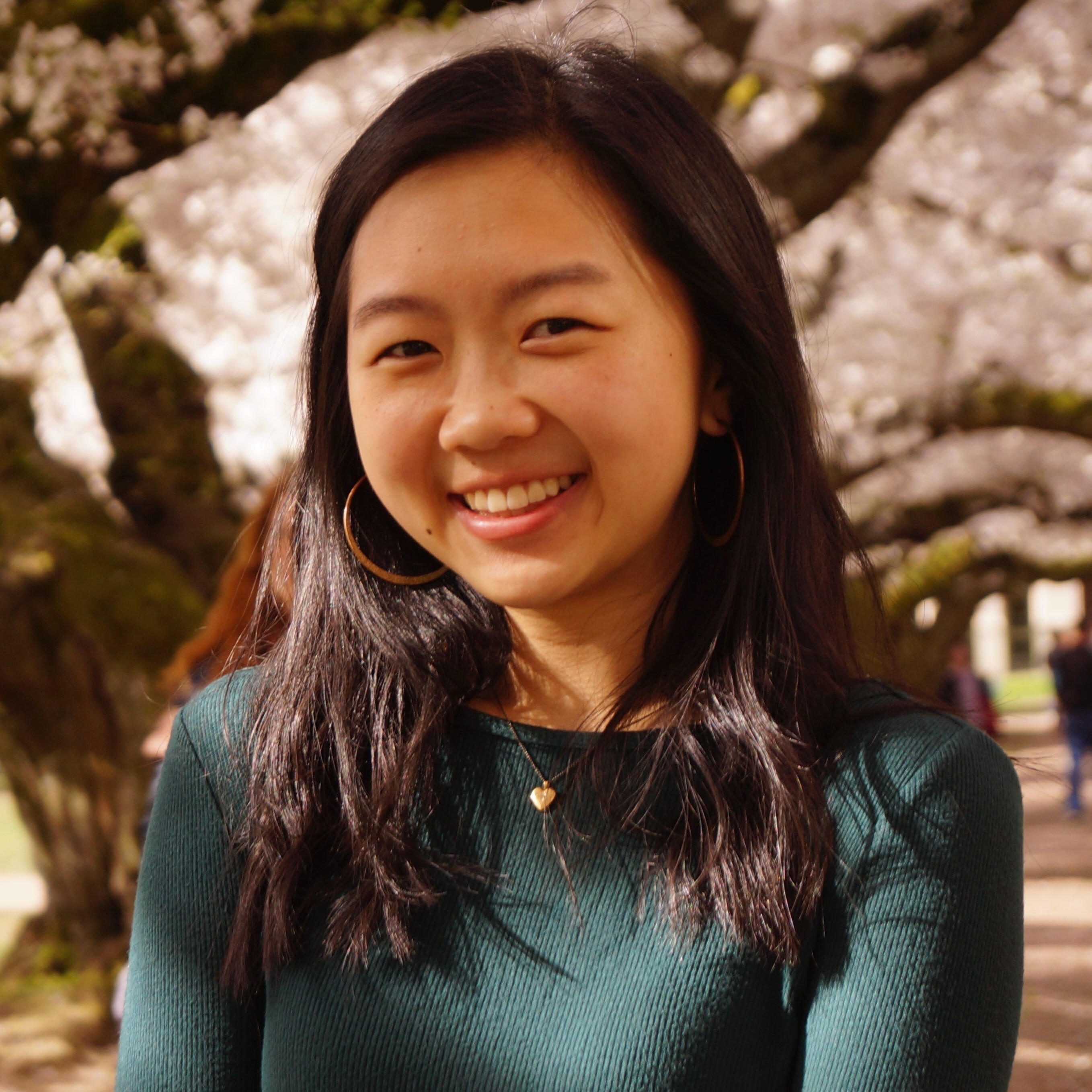 headshot of Linda, a Chinese Vietnamese womxn in her early 20’s with dark shoulder-length hair and gold hoops, smiling at camera